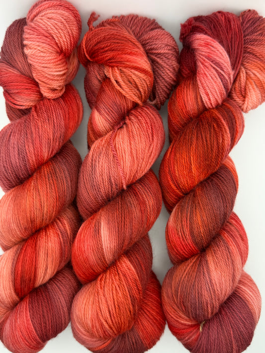 Three skeins of Japanese Fall hand dyed yarn in coral, burnt orange, brick red and wine