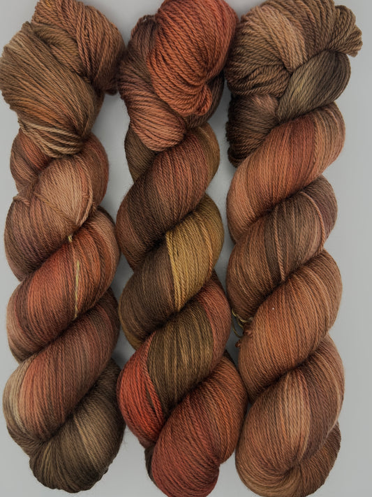 Three skeins of Autumn Getaway hand dyed yarn in copper, rust, chocolate brown, olive and mustard