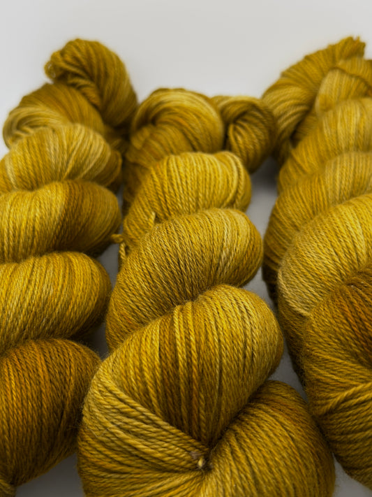 Old Gold hand dyed merino yarn skeins in tonal mustard and antique gold, beside the ancient gold coins that inspired the colourway